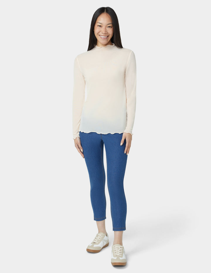 Woman wearing a cream mesh top and blue pants on a white background
