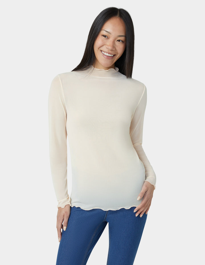 Woman wearing a sheer beige long-sleeve top over a blue outfit on a white background