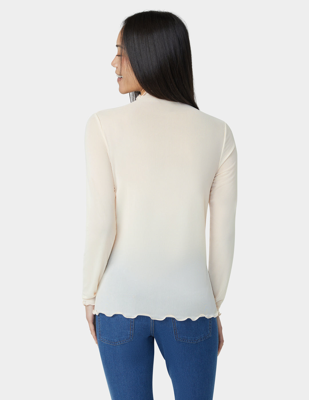 Woman wearing a cream-colored long-sleeve top with a scalloped hemline, standing against a white background.