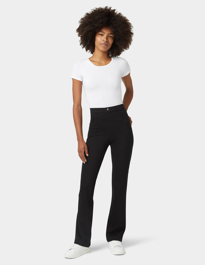 A model wearing bootcut black denim bottoms, paired with a white top and sneakers