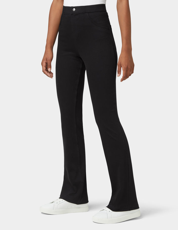 A model wearing black high-waisted flared pants with white sneakers, shown from the waist down against a light gray studio background.