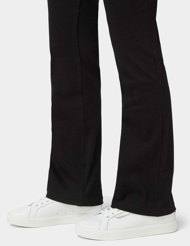 Black flared pants worn with white low-top sneakers, shown from the knees down on a light gray studio background.