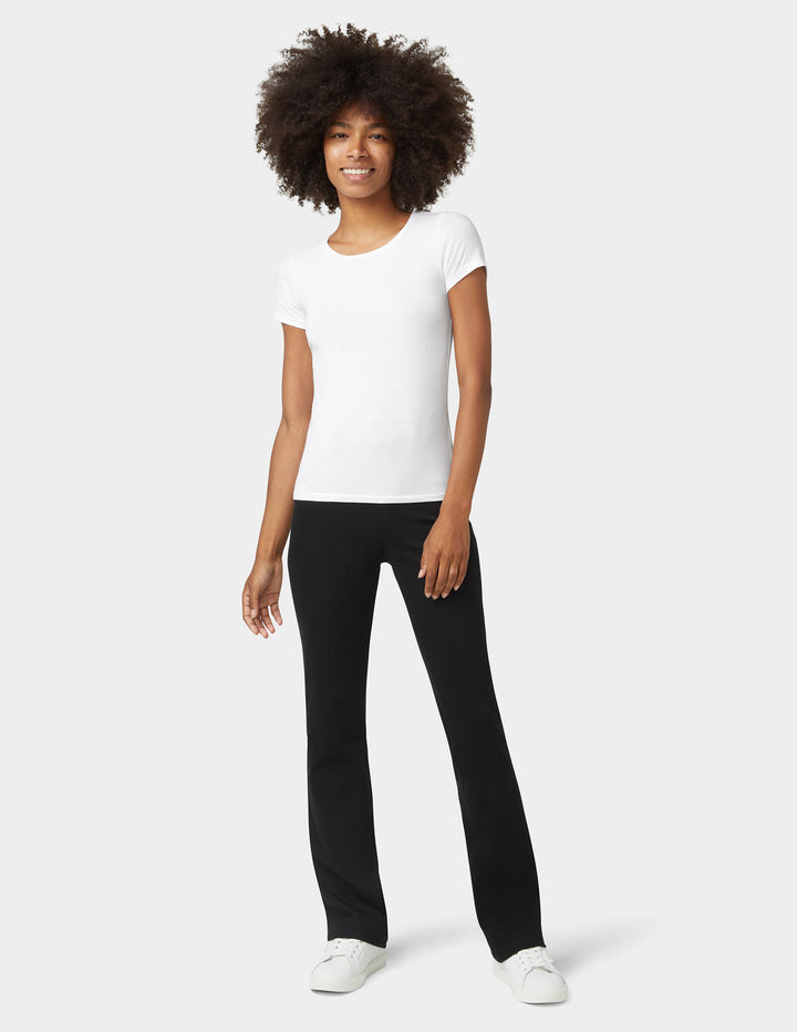 A model wearing bootcut black denim bottoms, paired with a white top and sneakers