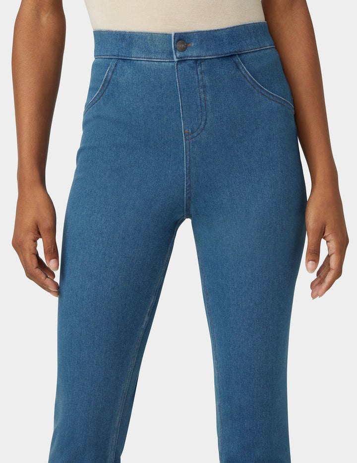 A close-up of a model wearing blue denim jeans with a high waist and front button closure, shown from the waist down against a light gray background.