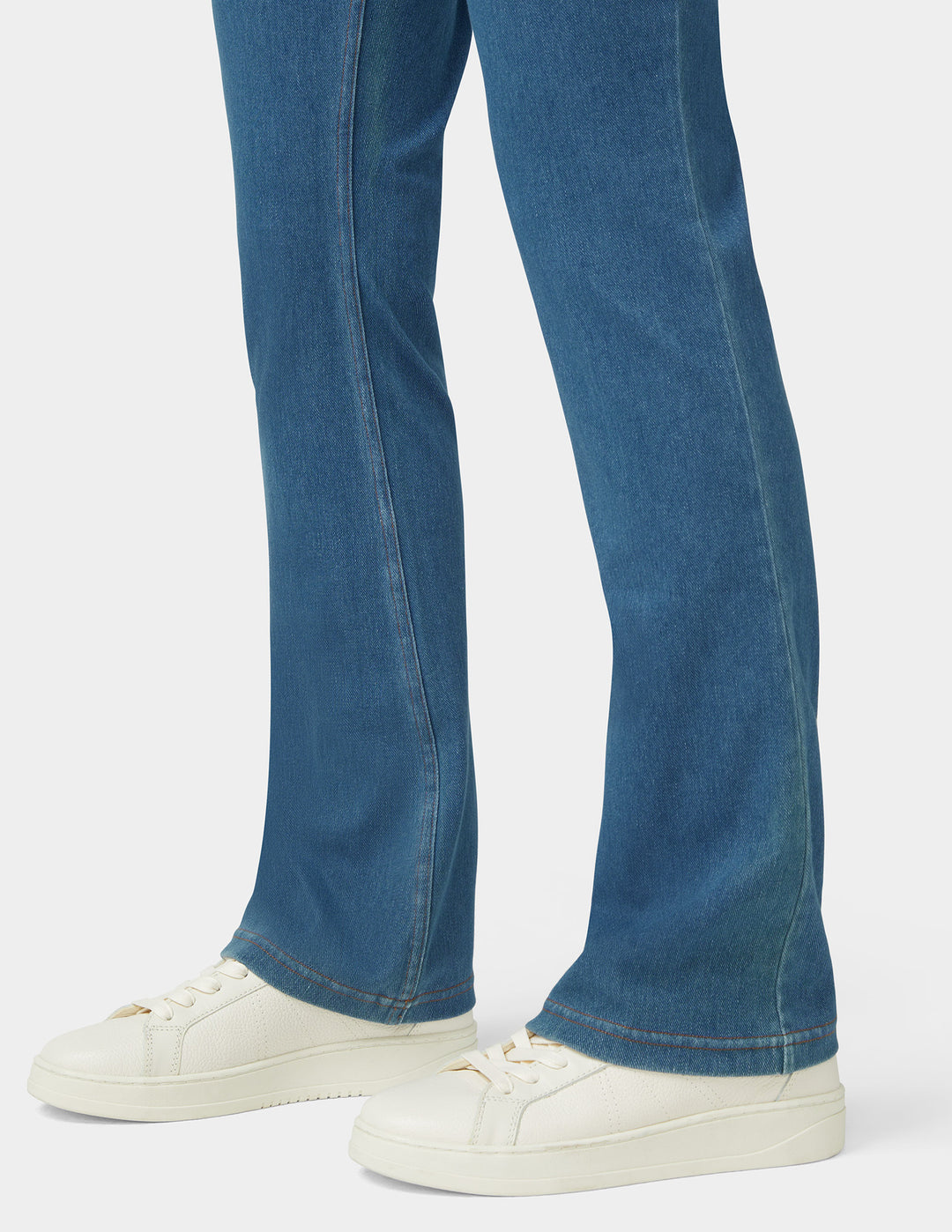 A model wearing bootcut blue medium wash bottoms from the knee down and white sneakers