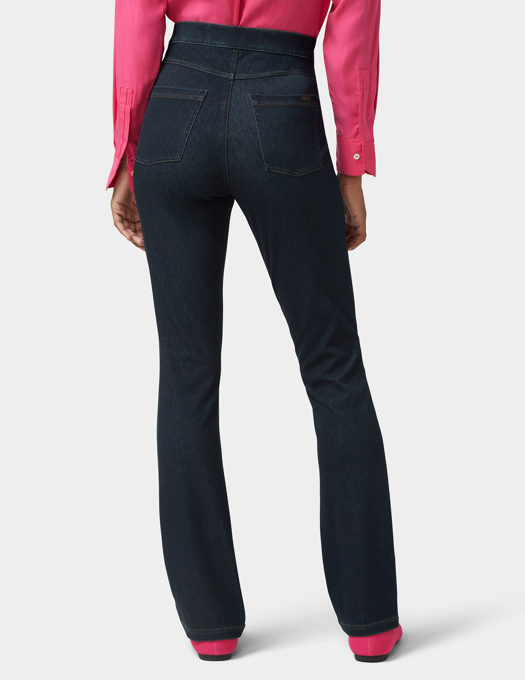 Woman wearing dark blue jeans with pink shoes on a light gray background