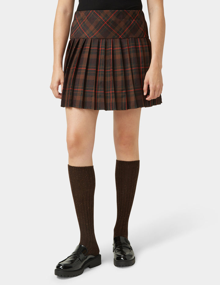 Person wearing a plaid skirt with knee-high socks and black shoes on a white background