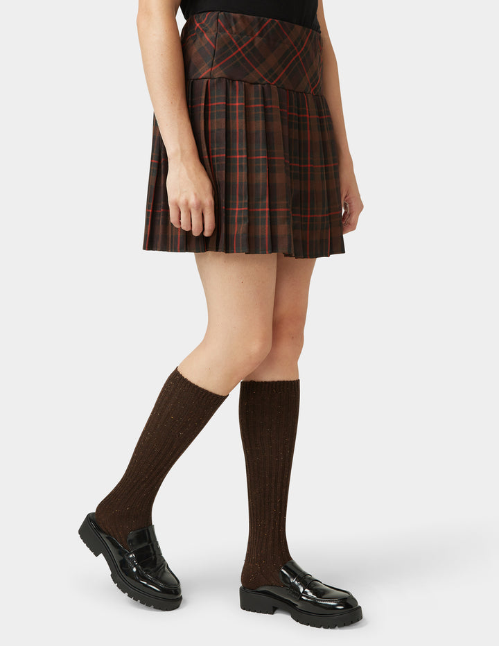 Person wearing a plaid skirt, brown knee-high socks, and black shoes on a white background