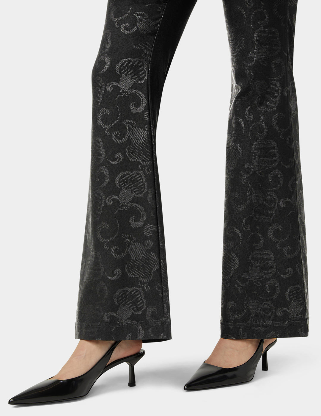 Black patterned pants worn with black high-heeled shoes on a white background
