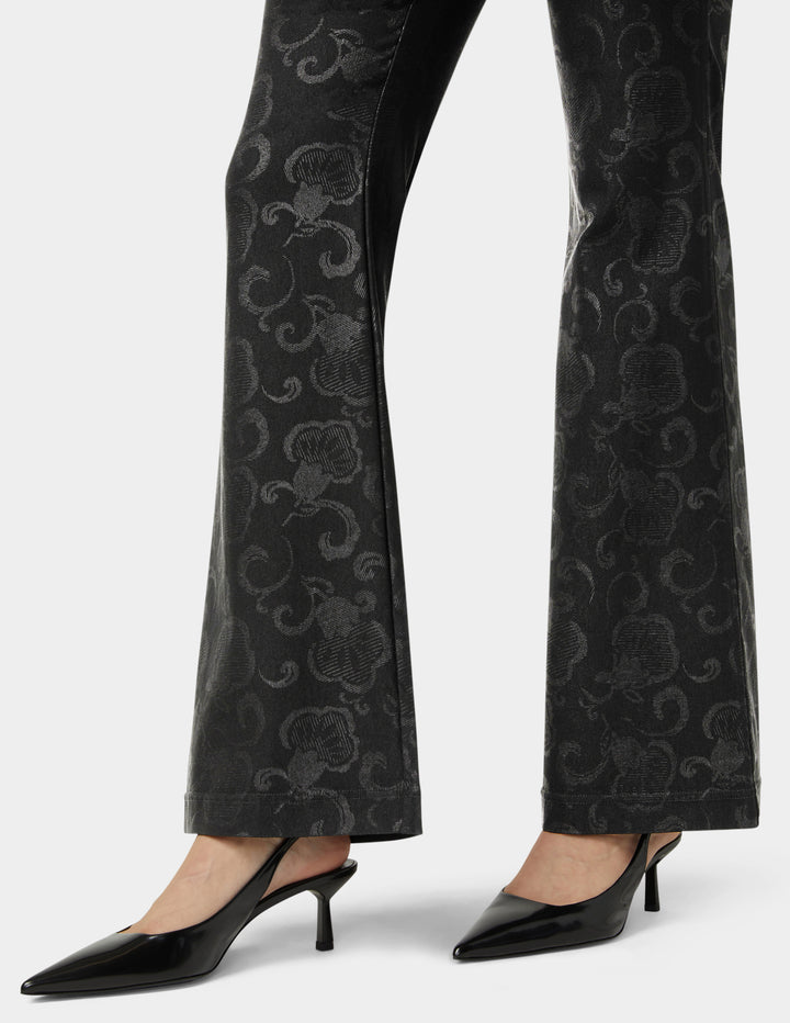 Black patterned pants worn with black high-heeled shoes on a white background