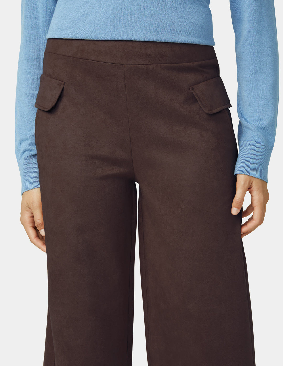 Brown pants worn with a light blue sweater on a plain background