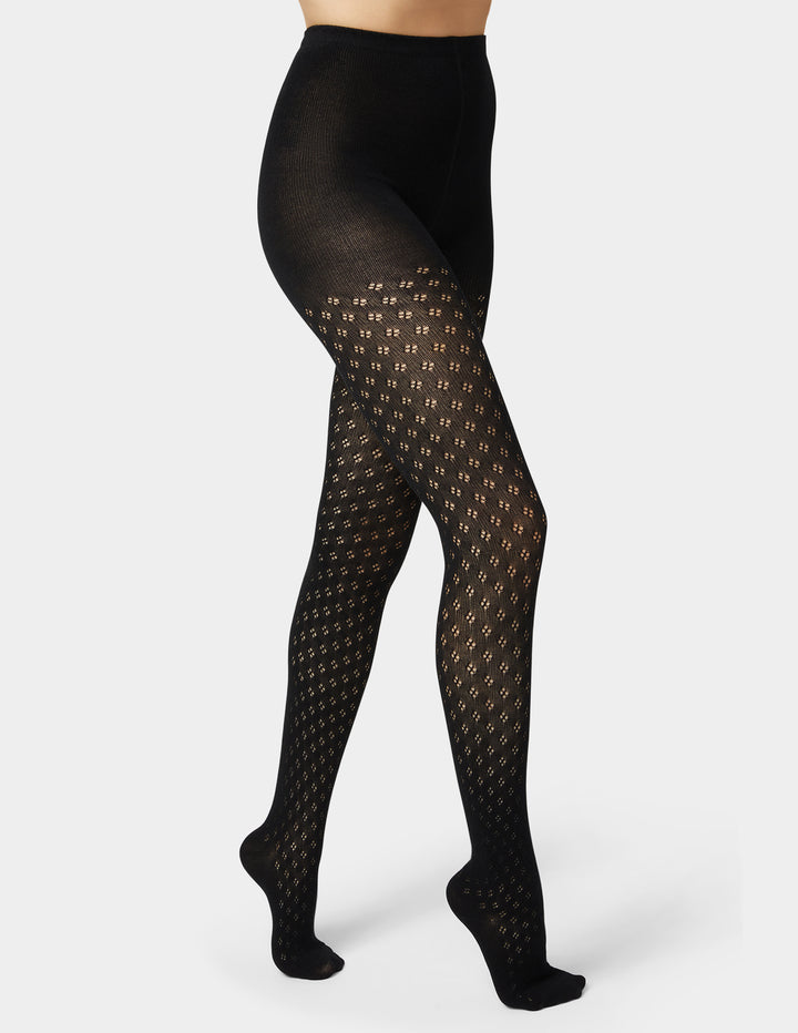 Woman wearing black pointelle sweater tights in black on grey background