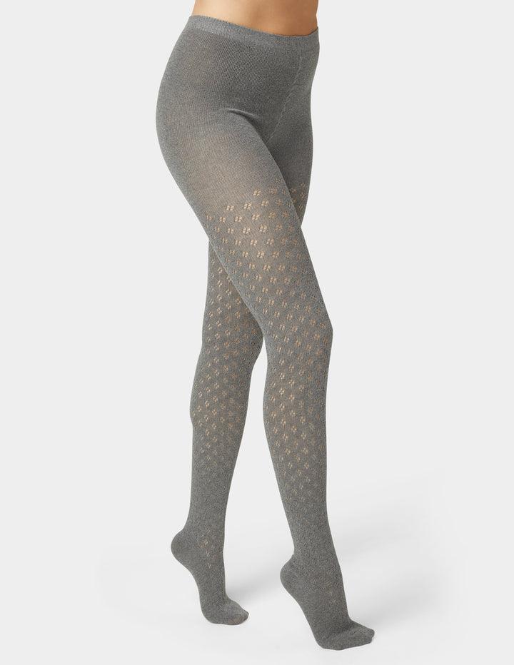 Woman wearing grey pointelle sweater tights in black on grey background
