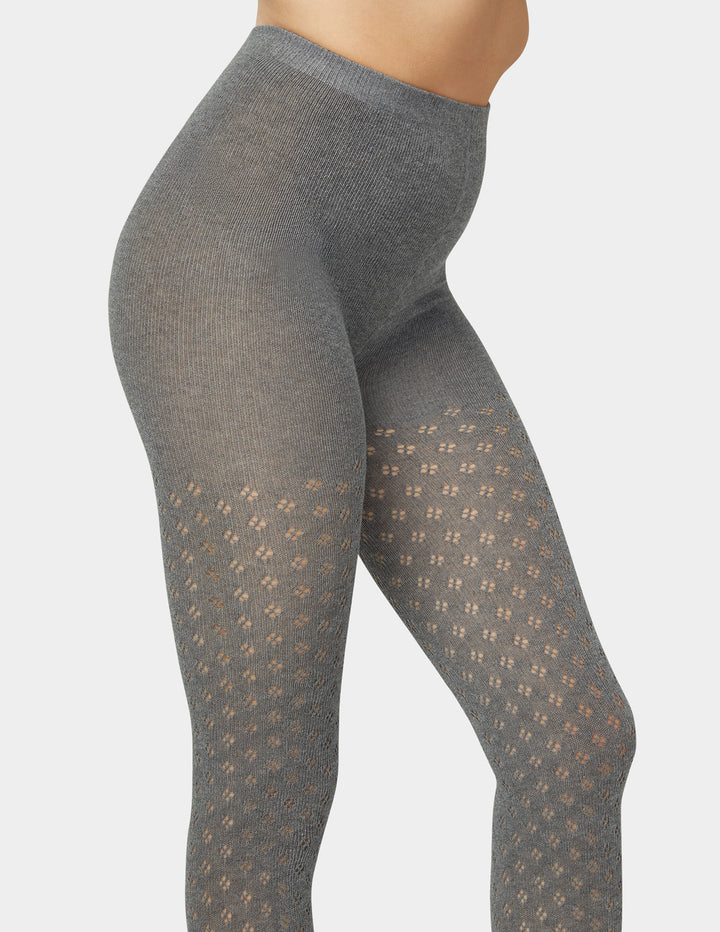 Woman wearing grey pointelle sweater tights in black on grey background