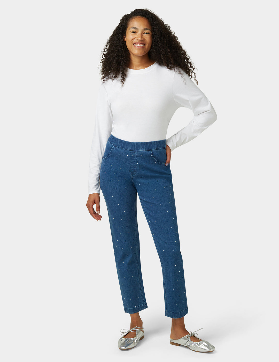 Woman wearing a white long-sleeve top and blue pants on a white background