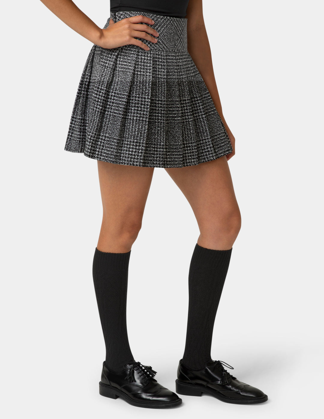 Person wearing a plaid skirt, black knee-high socks, and black shoes on a white background
