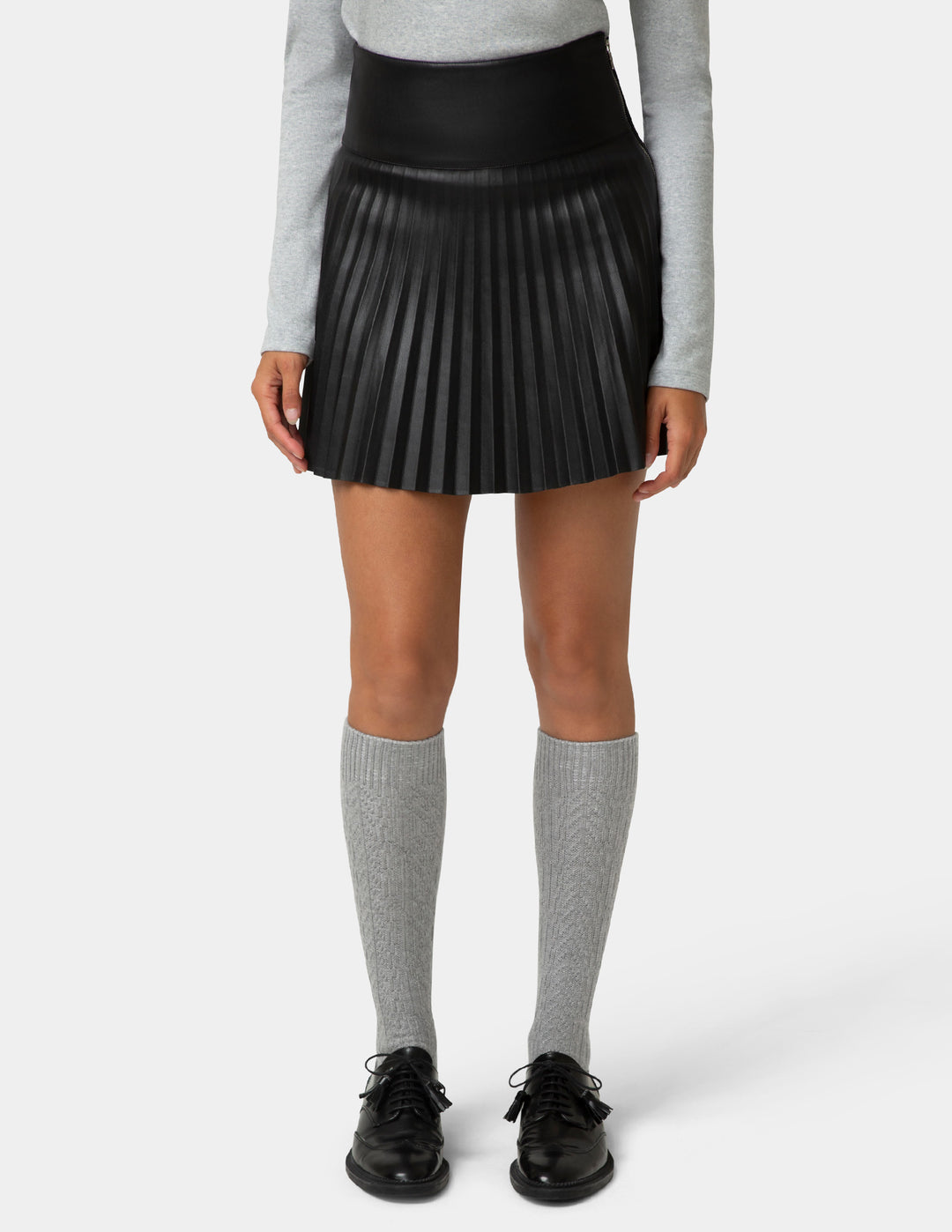 Person wearing a black pleated skirt, gray long-sleeve top, gray knee-high socks, and black shoes on a white background
