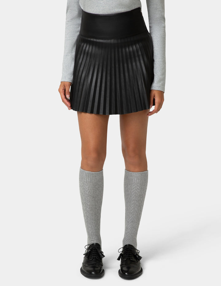 Person wearing a black pleated skirt, gray long-sleeve top, gray knee-high socks, and black shoes on a white background