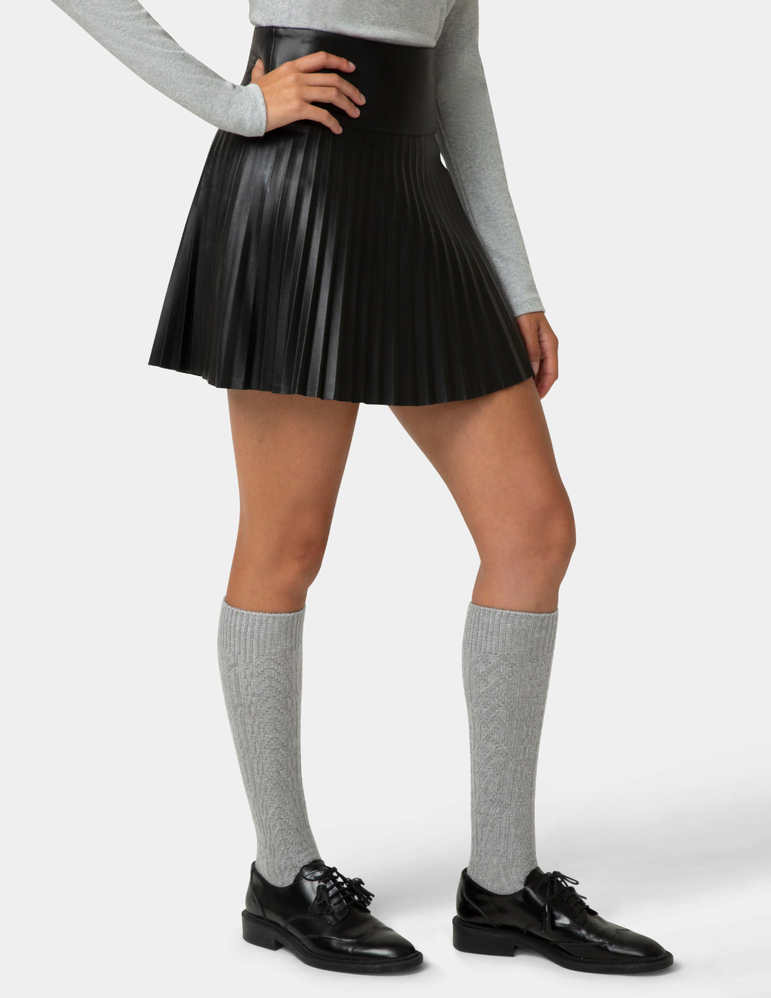 Person wearing a black pleated skirt, gray knee-high socks, and black shoes on a white background