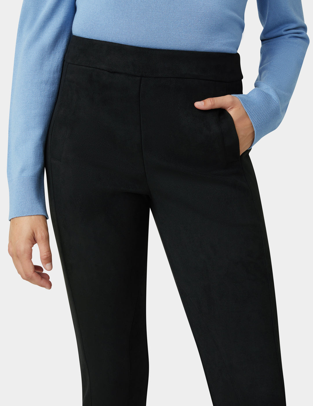 Person wearing black pants with a light blue long-sleeve top on a white background