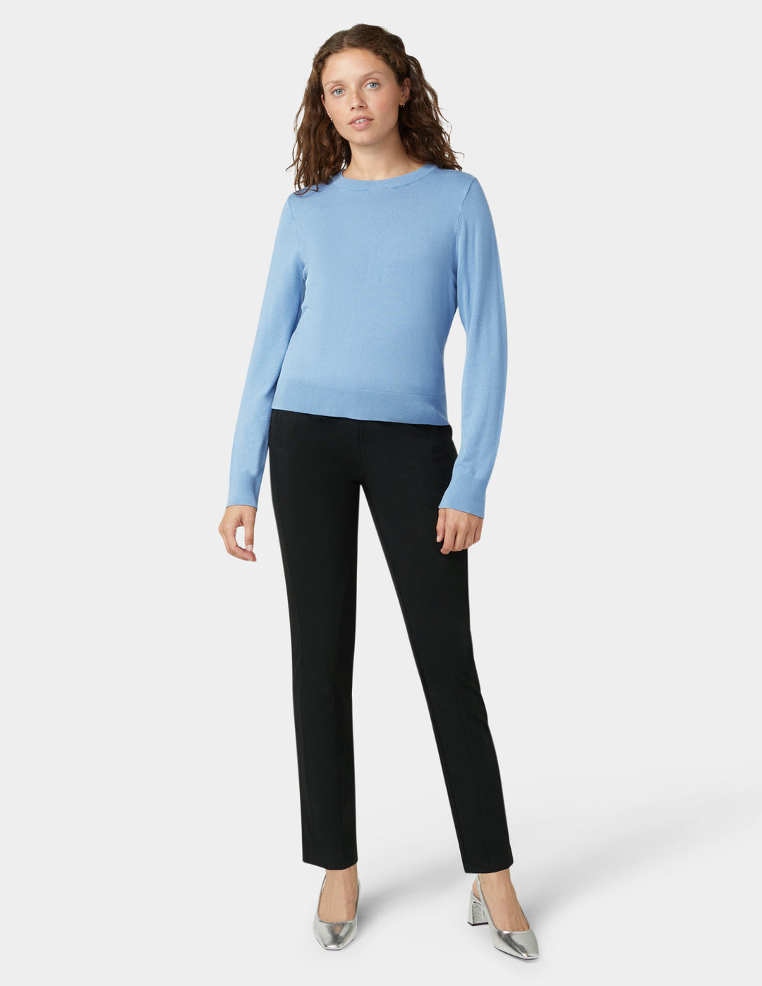 Woman wearing a light blue sweater and black pants on a white background