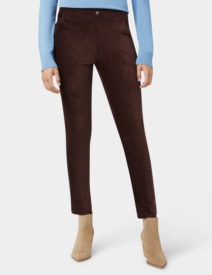 Brown corduroy pants worn with a light blue sweater and beige boots on a white background