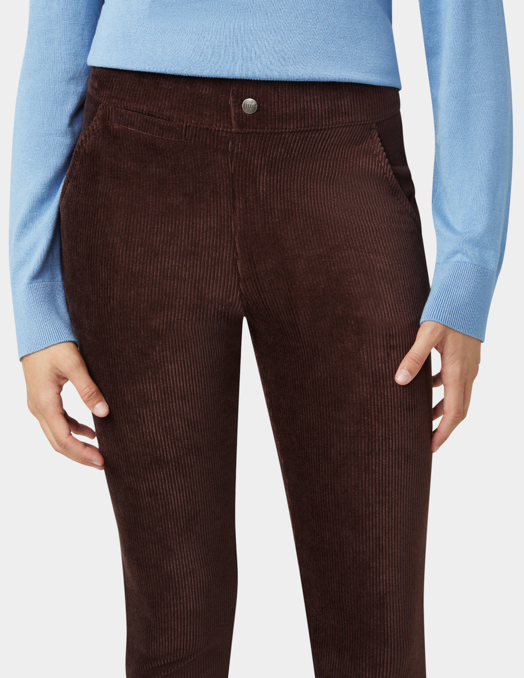 Brown corduroy pants worn with a light blue sweater on a white background