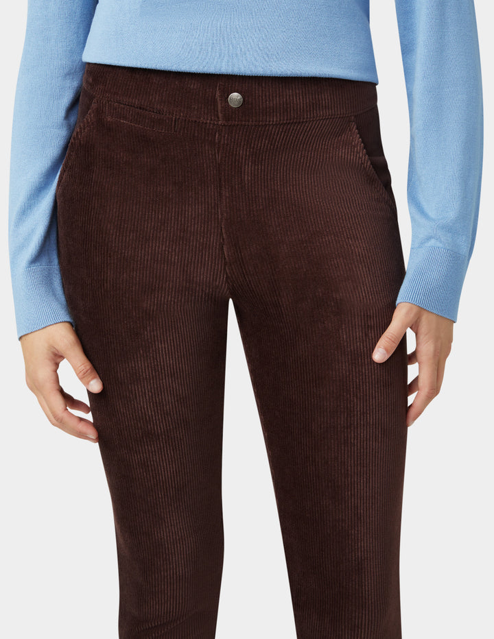 Brown corduroy pants worn with a light blue sweater on a white background