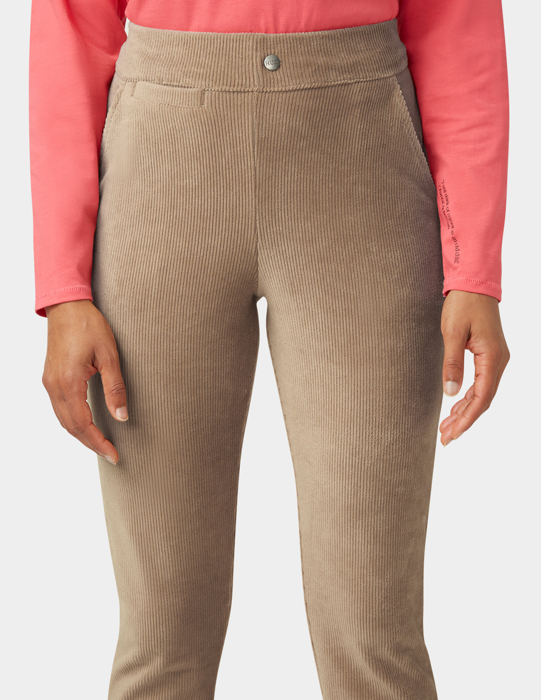 Beige corduroy pants worn with a pink long-sleeve shirt on a white background