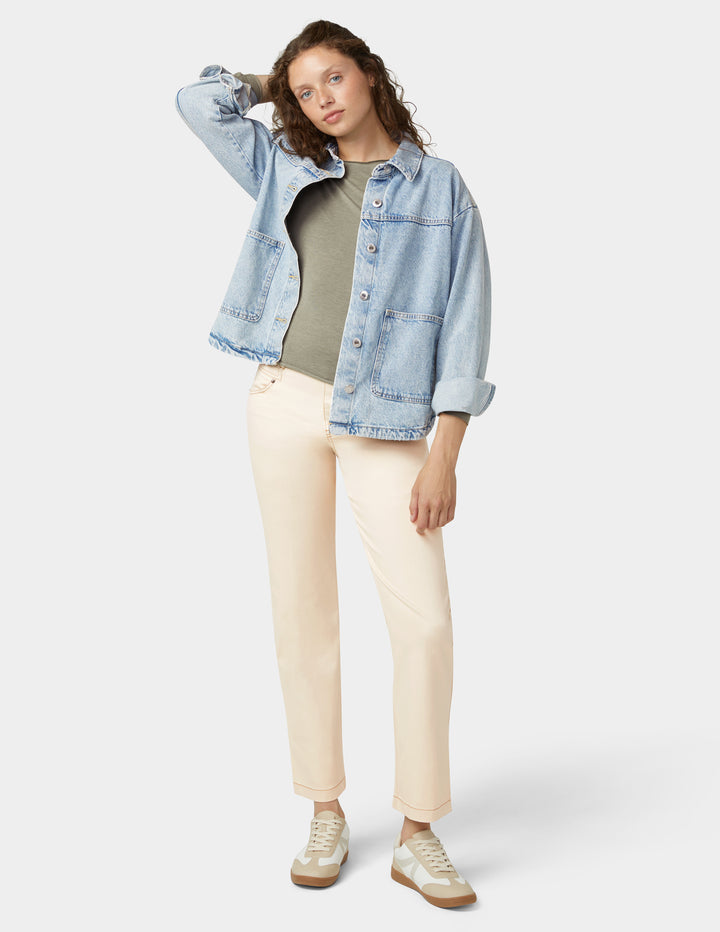 Woman wearing a light blue denim jacket, green shirt, beige pants, and white sneakers on a white background