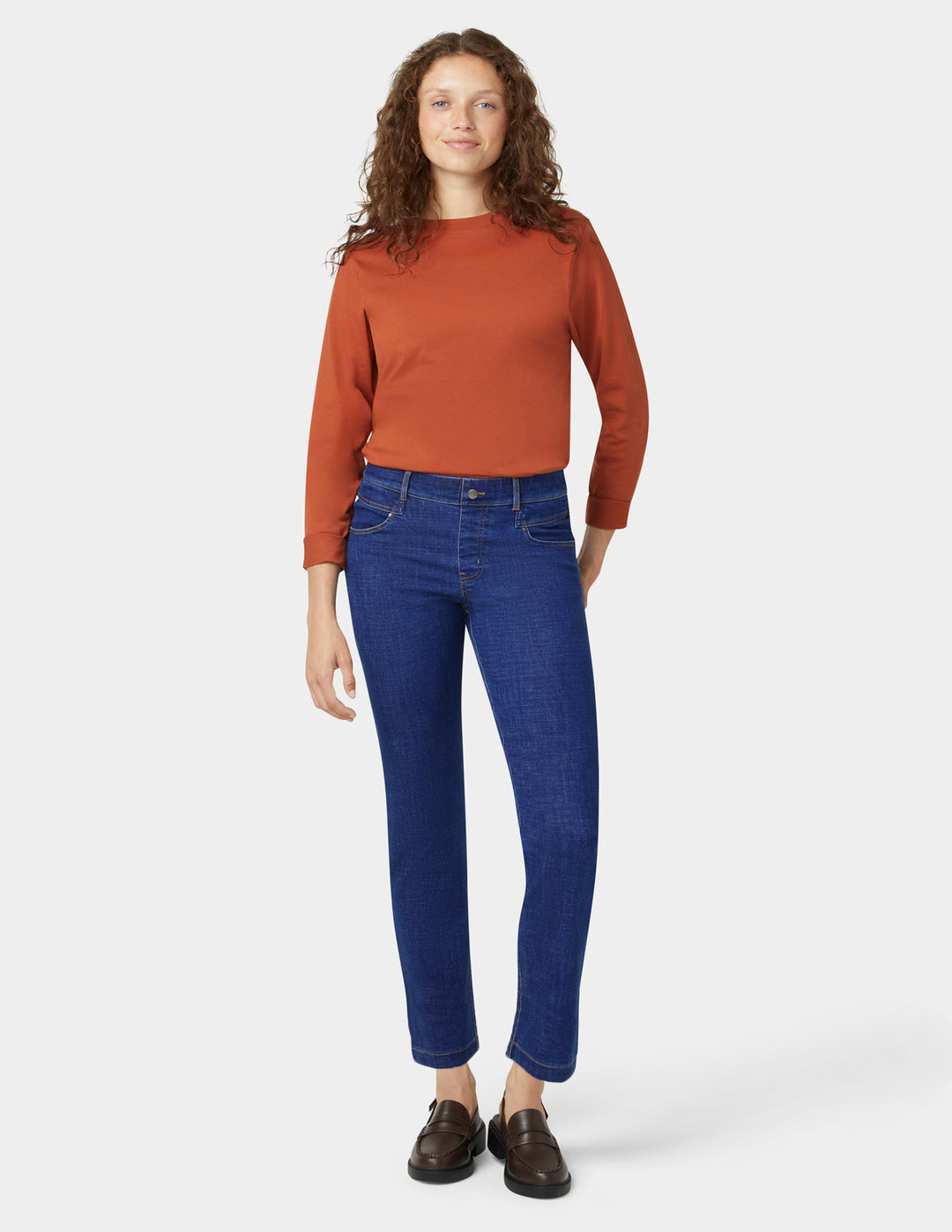 Woman wearing a rust-colored sweater and blue jeans on a white background