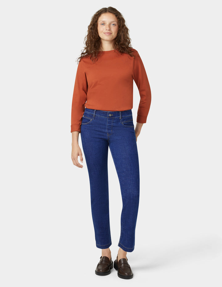 Woman wearing a rust-colored sweater and blue jeans on a white background