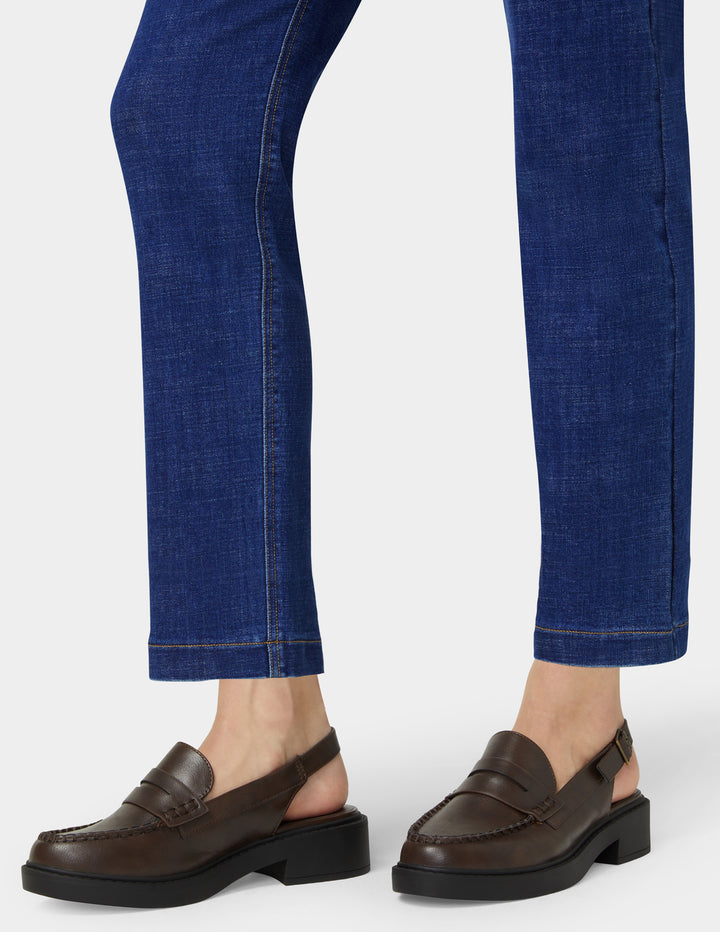 Brown loafers worn with blue jeans on a white background