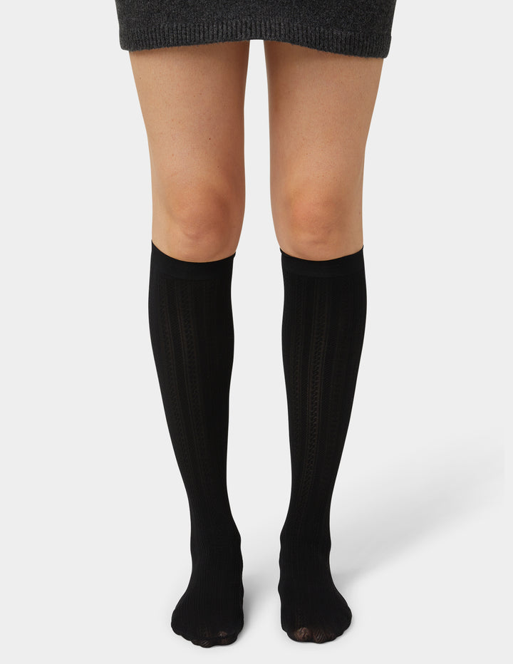 Black knee-high socks worn with a gray skirt on a white background