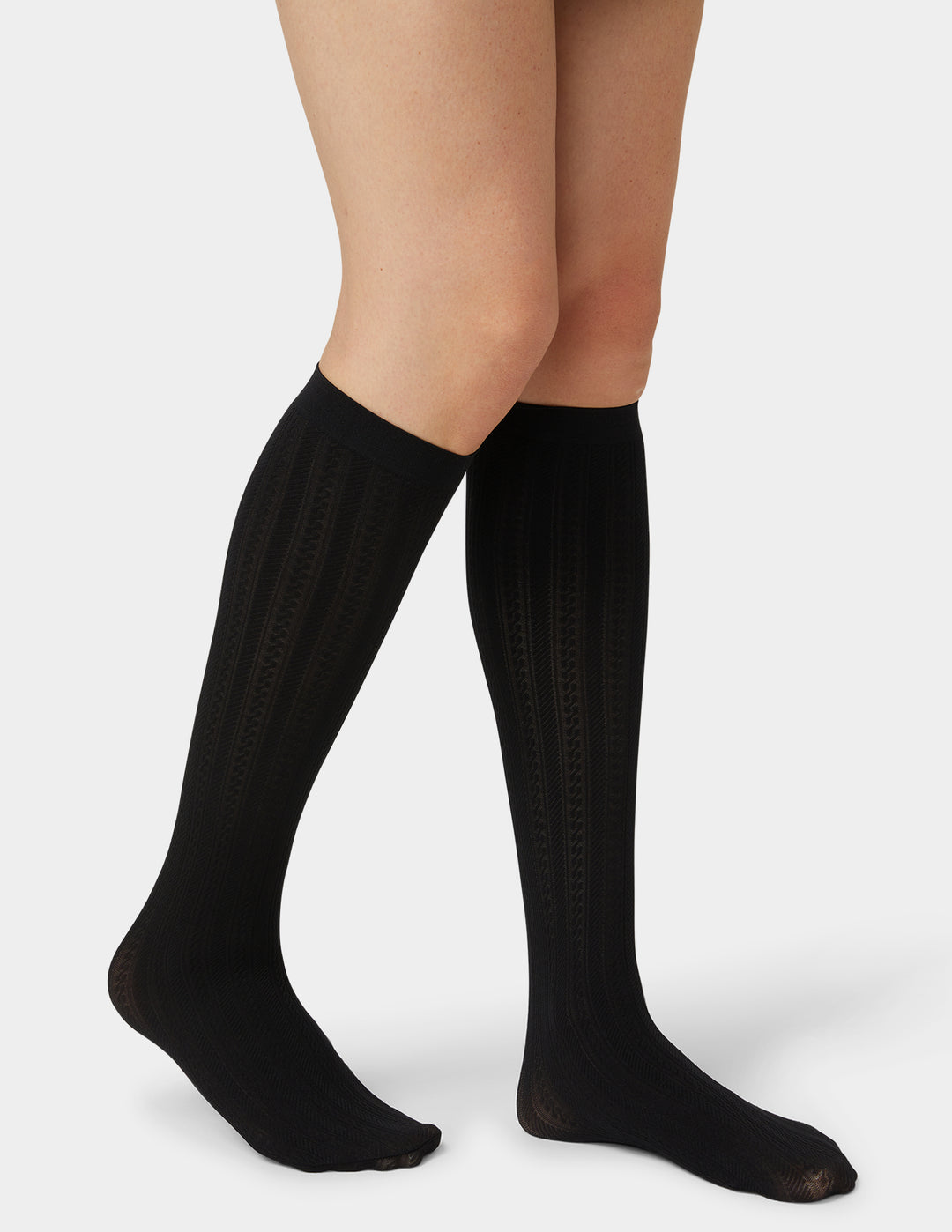 Black knee-high socks worn by a person on a light gray background