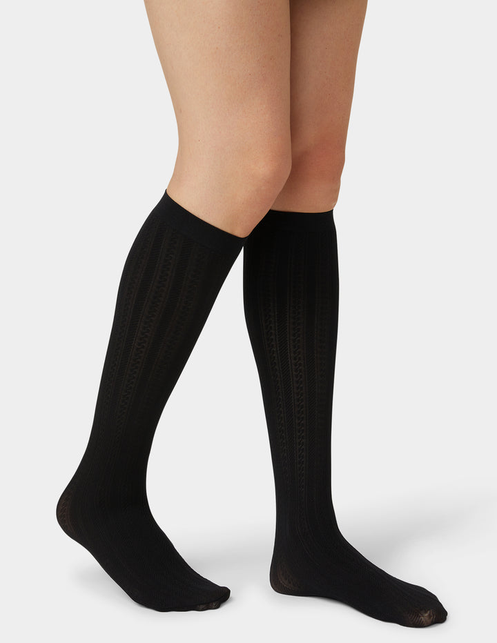 Black knee-high socks worn by a person on a light gray background