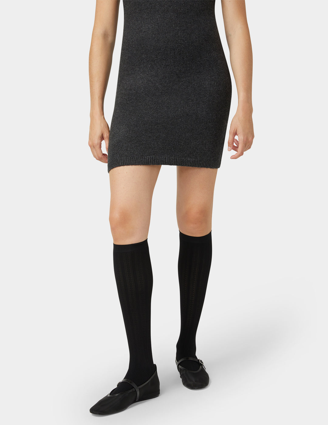 Person wearing a black knit dress with knee-high black socks on a white background