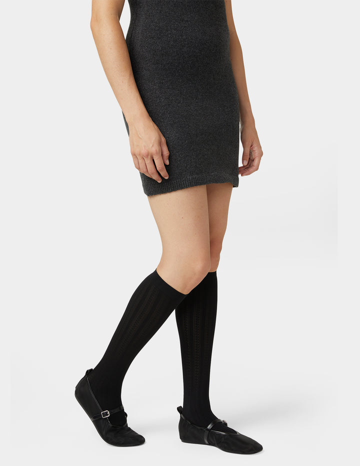 Person wearing a black dress, knee-high black socks, and black shoes on a white background