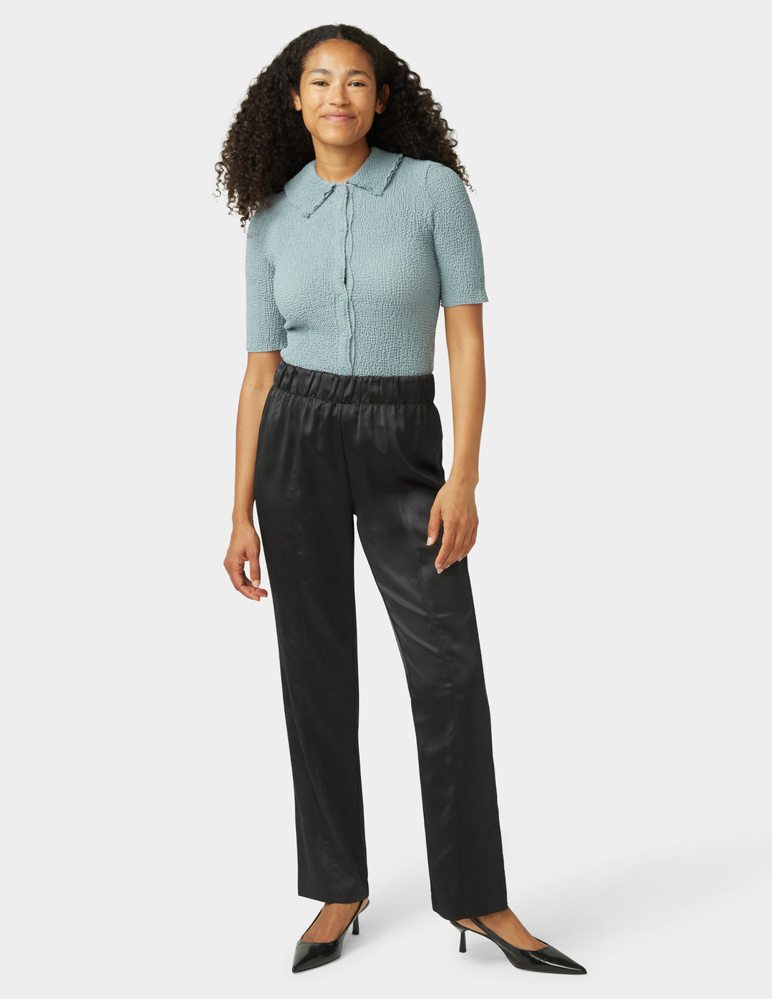 Woman wearing a light blue short-sleeve top and black pants on a white background