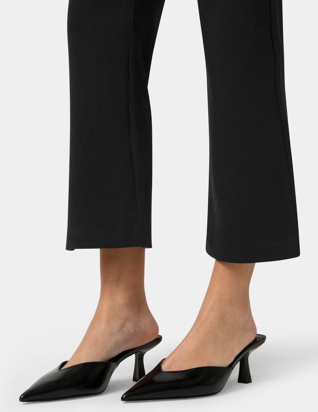 Black high-heeled shoes worn with black pants on a white background