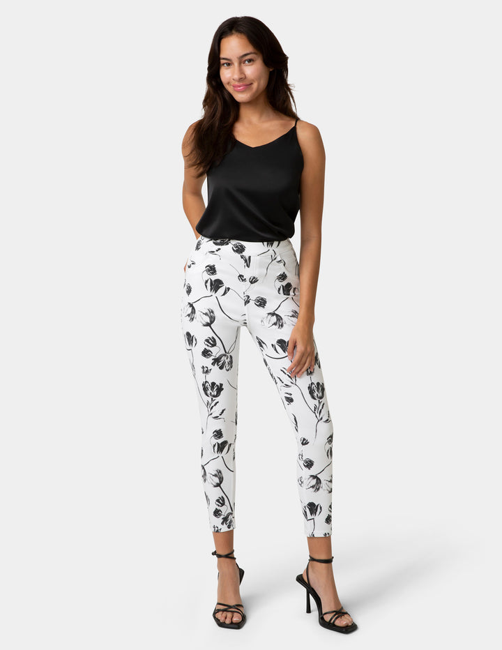 Woman wearing black tank top and white floral pants on a white background
