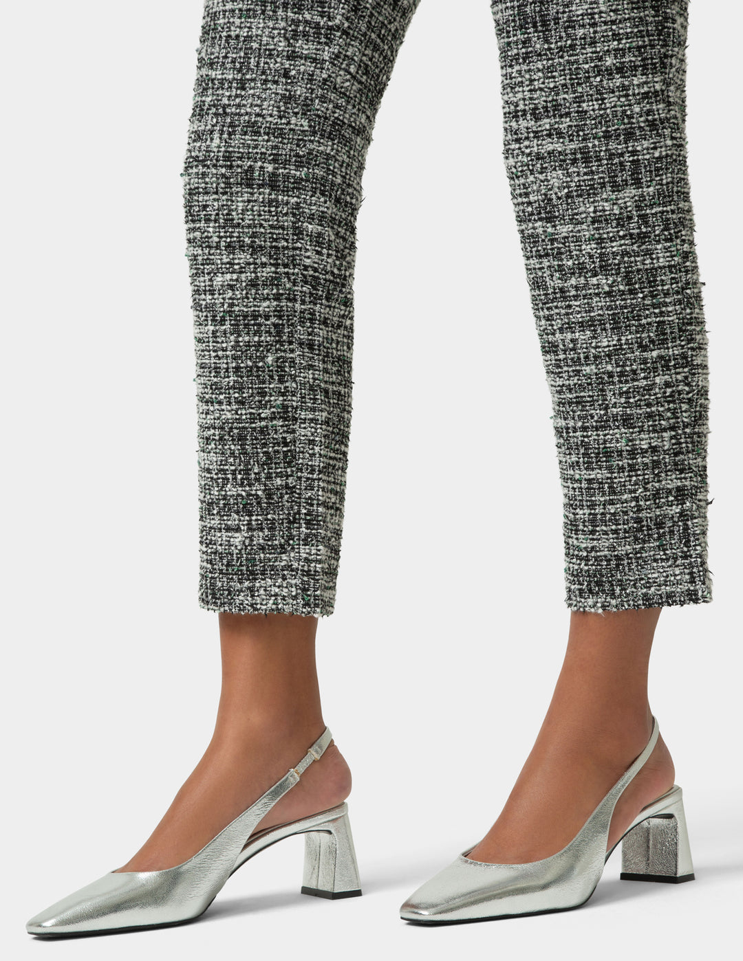 Silver high-heeled shoes worn with black and white patterned pants on a light gray background