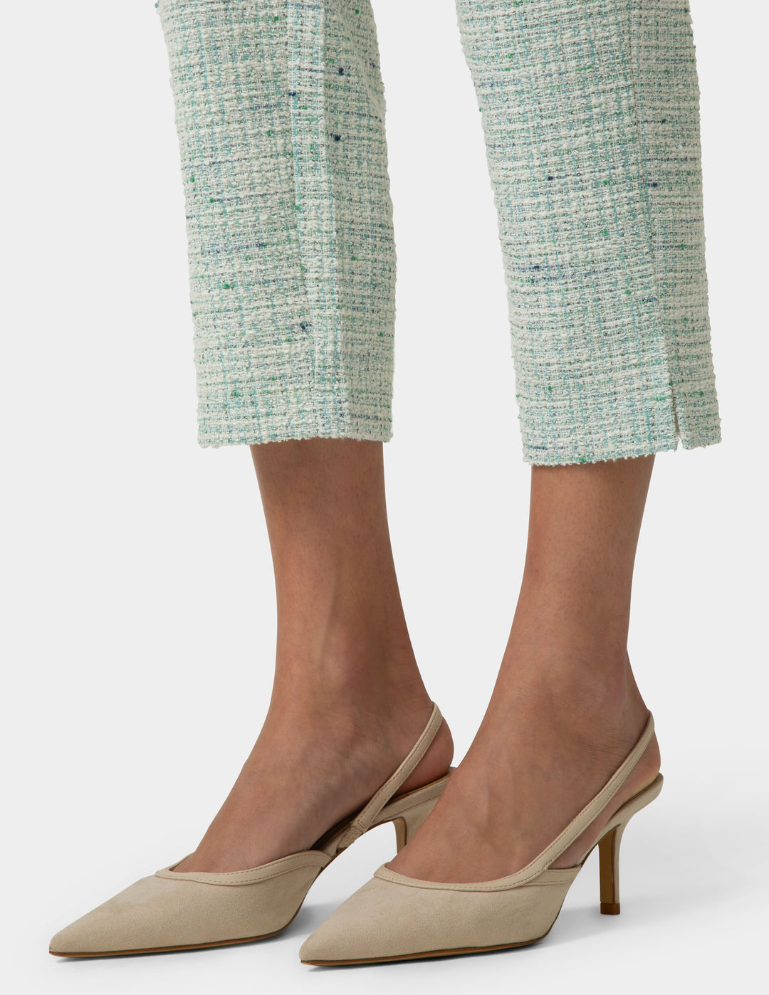 Beige high-heeled shoes worn with light green textured pants on a white background