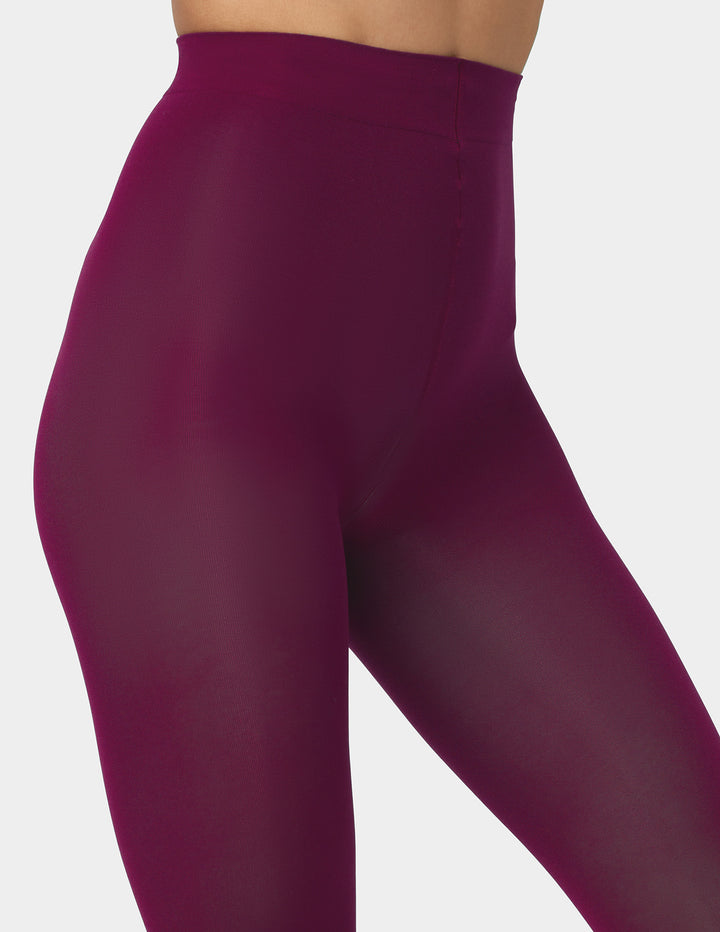 Close-up of a model wearing high-waisted, eggplant colored tights against a light gray background.